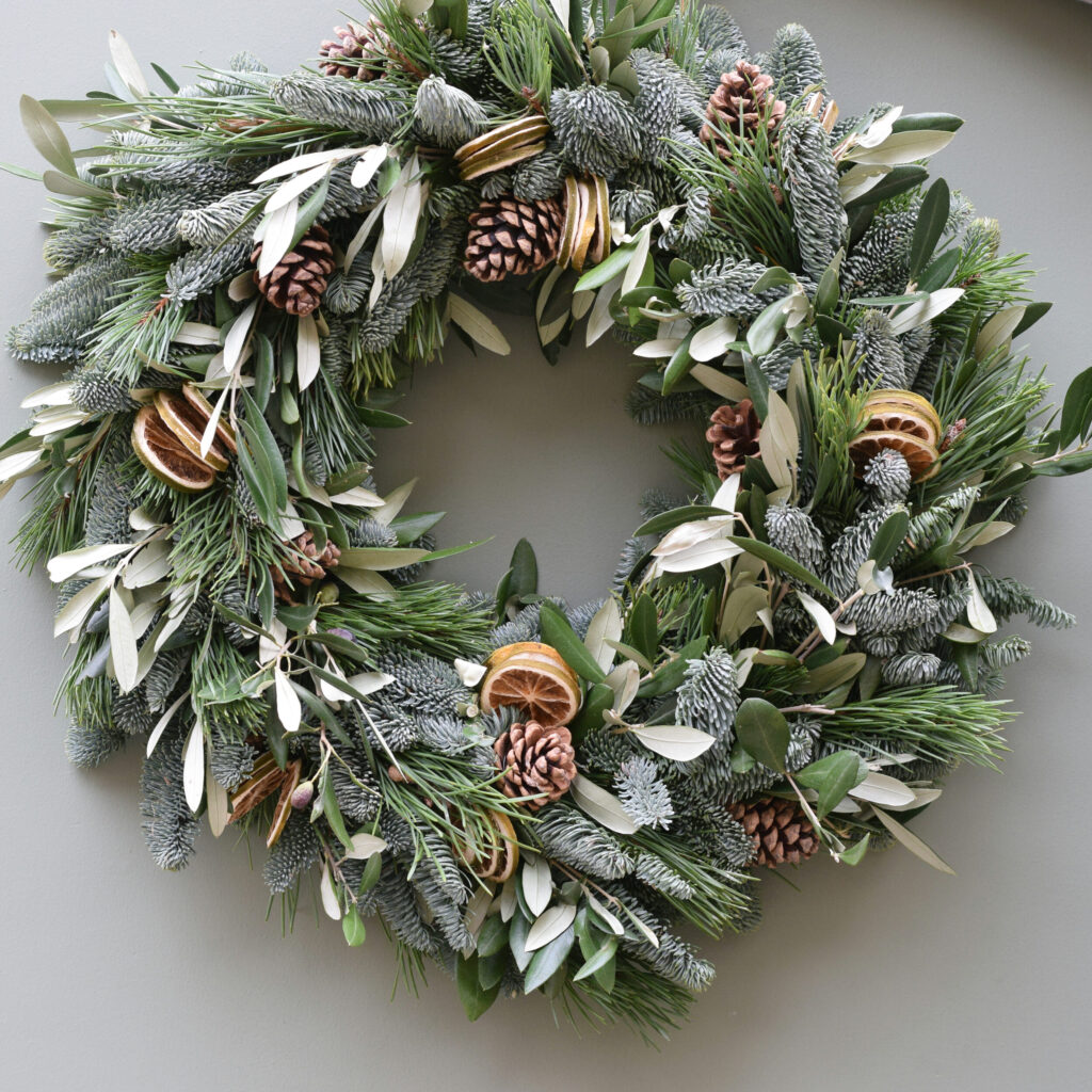 Sample of The Luxury Charlotte Christmas wreath, a Mix pine and olive foliage wreath, dressed with green dried fruit and pine cones, available to order from Kensington flowers London